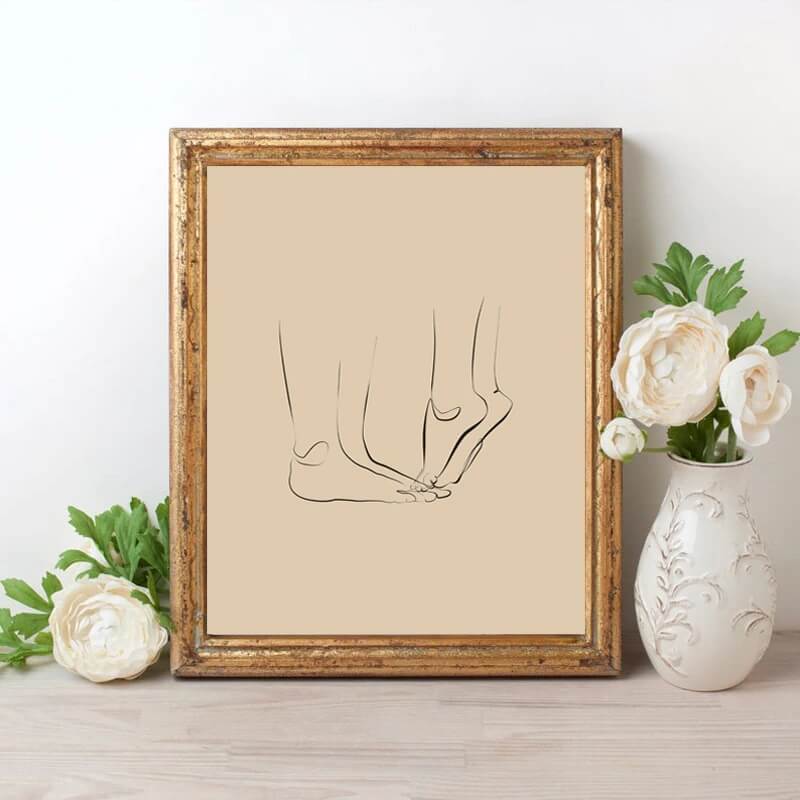 A canvas print of minimalist couple line art in black and white, displayed in a wooden frame, accompanied by white flowers in a vase.