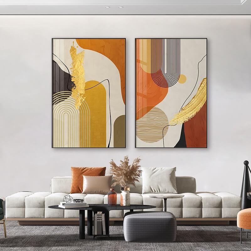 Two framed abstract geometric canvas prints with beige, gold, and multicolor elements displayed above a modern sofa in a living room setting.