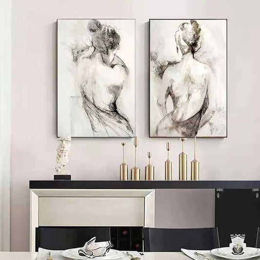 Two canvas wall art prints depicting abstracted, monochrome illustrations of a woman's back in a vintage style on a wall above a console table and decorative items.